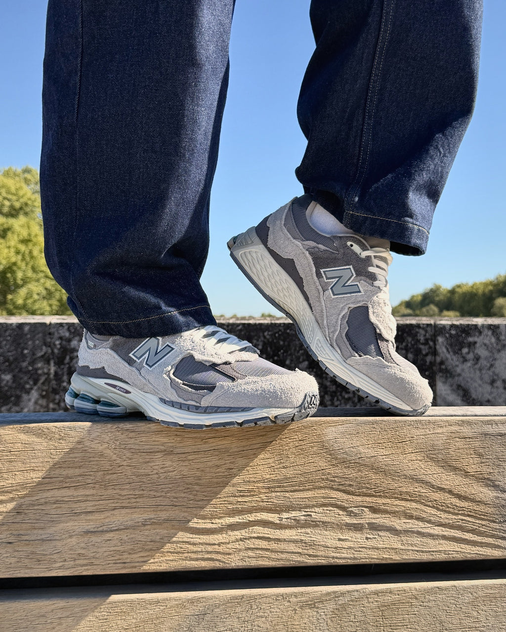 New Balance 2002R Protection Pack Rain Cloud portées en duo sur un banc